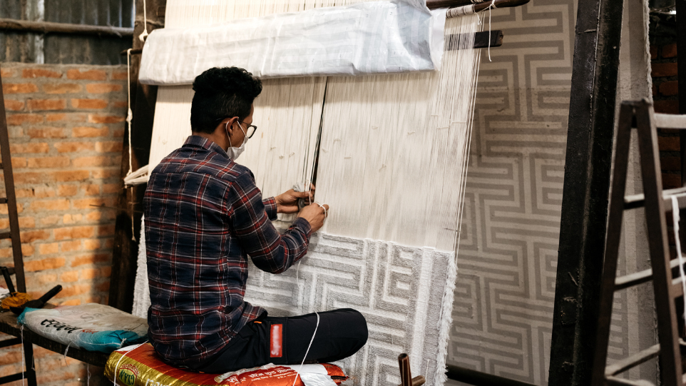 A carpet worker weaves on a large loom in Nepal. Photo credit: The Studio_M – thestudiom.com